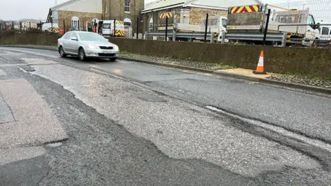 BBC A car drives past a series of large potholes