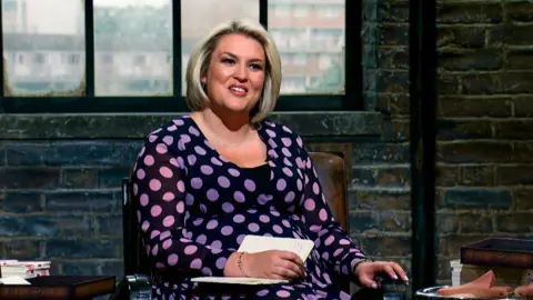 BBC Sara Davies sat down on the set of Dragons' Den wearing a black dress with purple spots