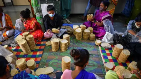 Getty Images In this photograph taken on March 8, 2021, members of Shri Mahila Griha Udyog, the organisation that produces the famous Lijjat Papad, arrange rolled papadums for delivery at one of the organisation's facilities in Mumbai. - The fairytale success of Lijjat Papad -- a multi-million-dollar venture founded by seven women in a crowded Mumbai tenement in 1959 with seed capital of 80 rupees (1.10 USD) -- belies its revolutionary feminist aspirations. - TO GO WITH India-economy-gender-food, FEATURE by Ammu KANNAMPILLY (Photo by Indranil MUKHERJEE / AFP) / TO GO WITH India-economy-gender-food, FEATURE by Ammu KANNAMPILLY (Photo by INDRANIL MUKHERJEE/AFP via Getty Images)
