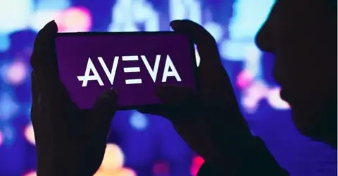 SOPA Images/Getty Images A silhouette of a person holding a phone with the Aveva logo on it