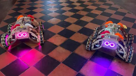 BBC Two small robots with glowing headlight eyes on the floor of St George's Church in Gravesend