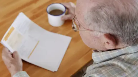 Getty Images A man looks at his energy bills while drinking something from a mug