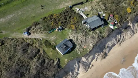 Martin Barber/BBC Drone picture shows two homes near the cliff edge at Hemsby beach