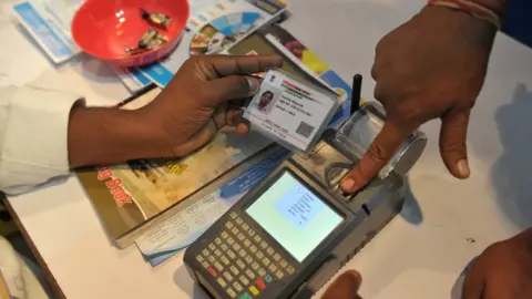 Getty Images An Indian visitor gives a thumb impression to withdraw money from his bank account with his Aadhaar card.