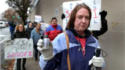 Getty Images Alec Smith's mother holds a vial of her son's ashes during a protest against the high price of insulin outside Sanofi's offices in Massachusetts