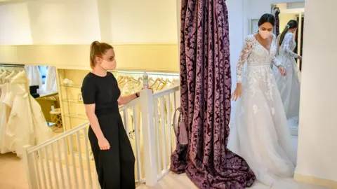 PA Media Jessica Letheren exits the fitting room after changing into a wedding dress assisted by bridal consultant Felicity Gray at Allison Jayne Bridalwear in Clifton, Bristol, which has reopened following the lifting of coronavirus lockdown restrictions, with measures put in place to prevent the spread of coronavirus during brides" dress fittings
