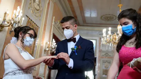 EPA Groom Iker (R) places a wedding ring on the hand of bride Aranzazu (L) as the bridesmaid (R) looks on during their civil wedding at the town hall of Alcala de Henares, Madrid, Spain, 06 June 2020. The nuptial ceremony was one of the first held there since the the state of emergency was implemented in March throughout Spain due to the pandemic COVID-19 disease caused by the SARS-CoV-2 coronavirus.