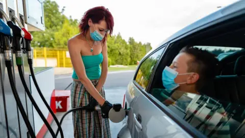Getty Images Woman filling up car with petrol with a child sitting in the car.