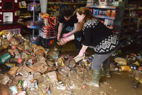 Getty Images Shop workers clearing rubbish from a flooded store in Cockermouth in December, 2015