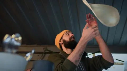 Nick Hartley/BBC Man throwing a pizza