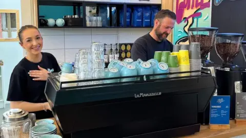Khaos Cakery/Facebook A young woman and a man work behind the coffee machine at Khaos Cakery in Auckland