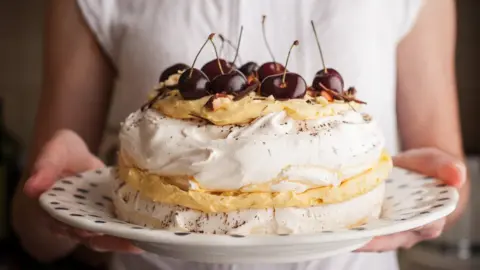 KarpenkovDenis A pavlova with cherries on top is seen on a plate held by a woman