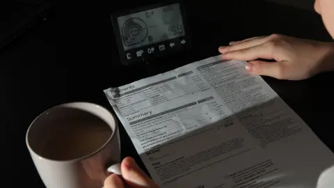 PA Media An energy bill being read next to a smart meter