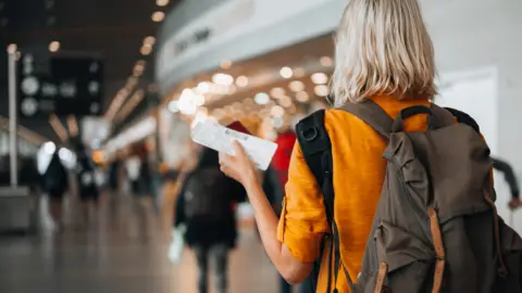 Getty Images Woman at the airport holding a passport with a boarding pass.
