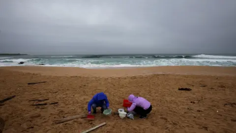 Reuters Women clean up the sand of Vilar beach