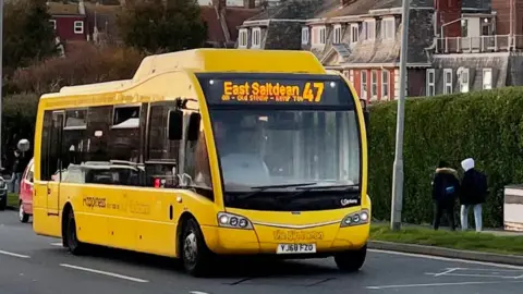 The Big Lemon a yellow bus with East Saltdean 47 written on a digital board at the front passes along a road