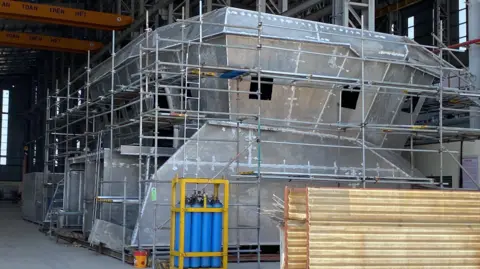 Isles of Scilly Steamship Group Unpainted steel wheelhouse of new vessel surrounded by scaffolding. It is sitting in a boatyard shed in Vietnam yet to be lowered on to the vessel