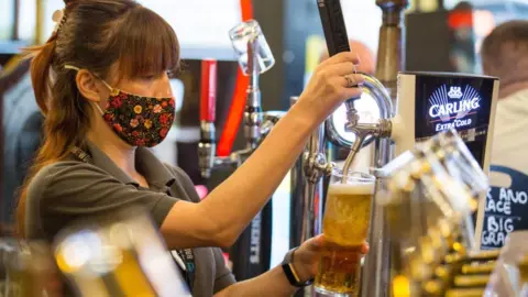 Getty Images Woman wearing facemask pours a pint